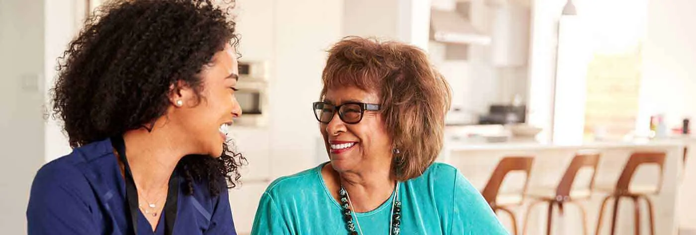 Young African-American health assistant talking with smiling senior African-American woman