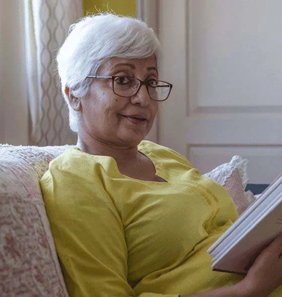 Asian-American senior woman reading a book wearing a yellow shirt with glasses