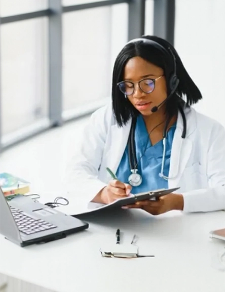 African-American female doctor working at computer while taking phone call with member