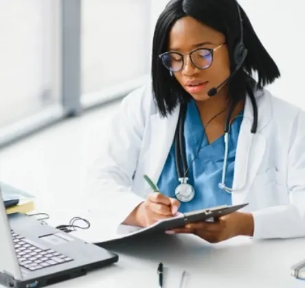 African-American female doctor working at computer while taking phone call with member African-American female doctor working at computer while taking phone call with member