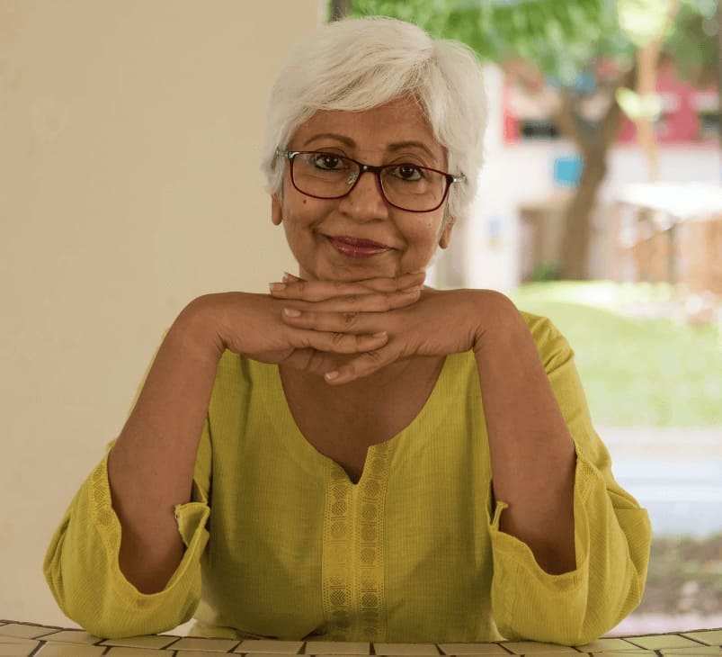 Senior Asian-American woman with hands crossed smiling and sitting at table